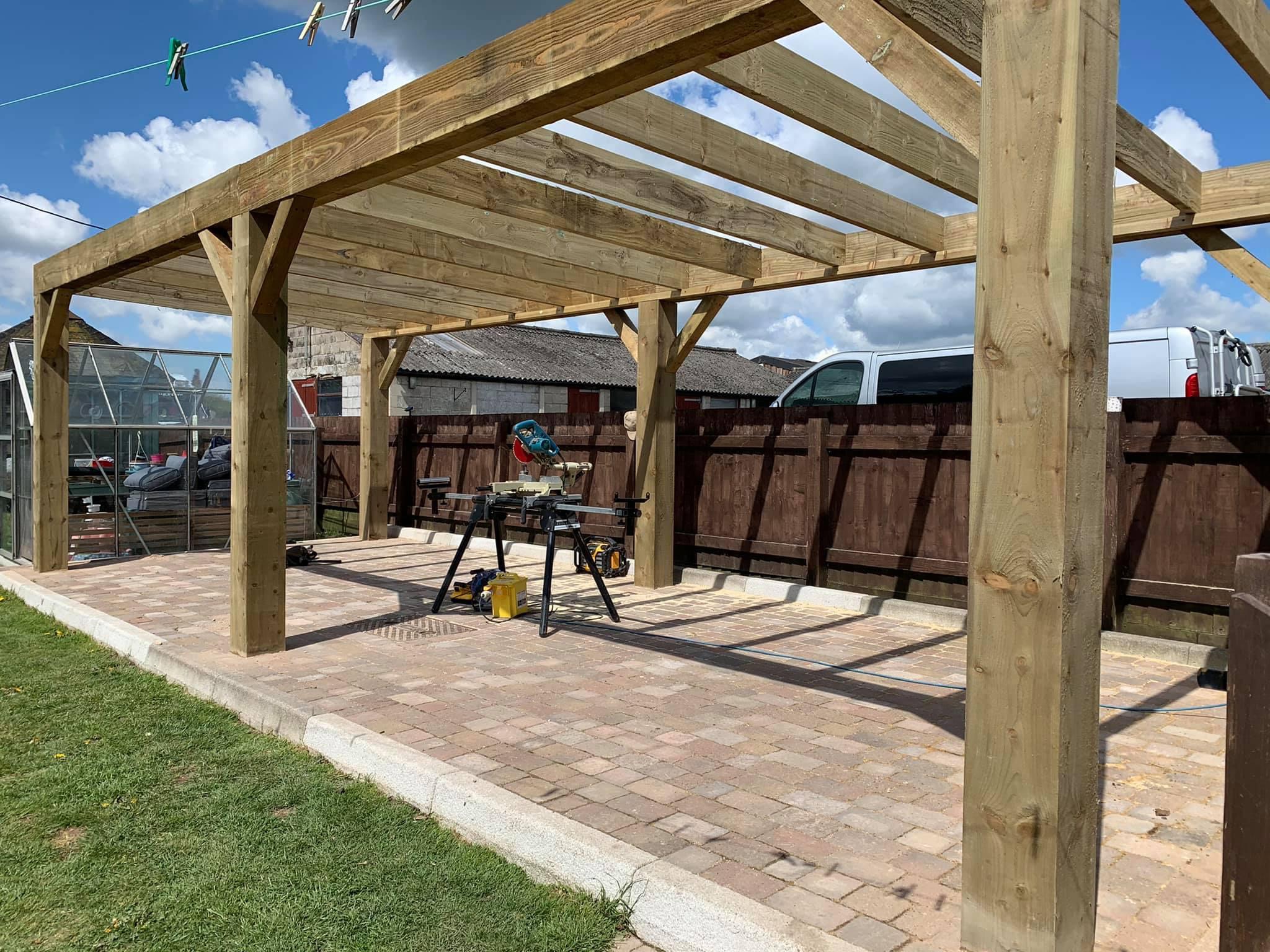 Timber-frame pergola going up over a block-paved patio